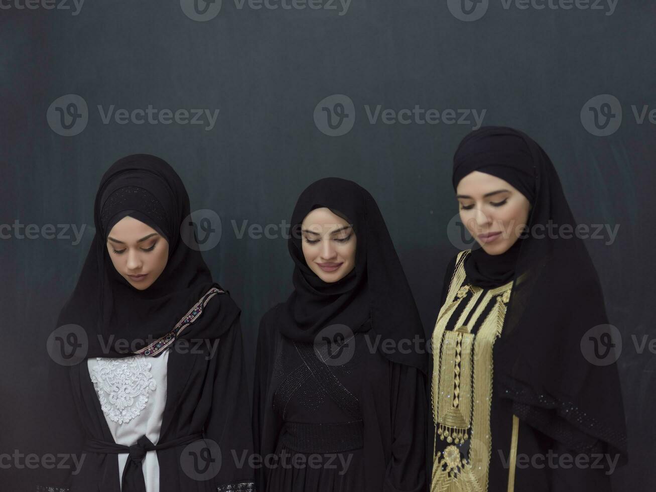Group portrait of beautiful Muslim women in a fashionable dress with hijab isolated on black background photo