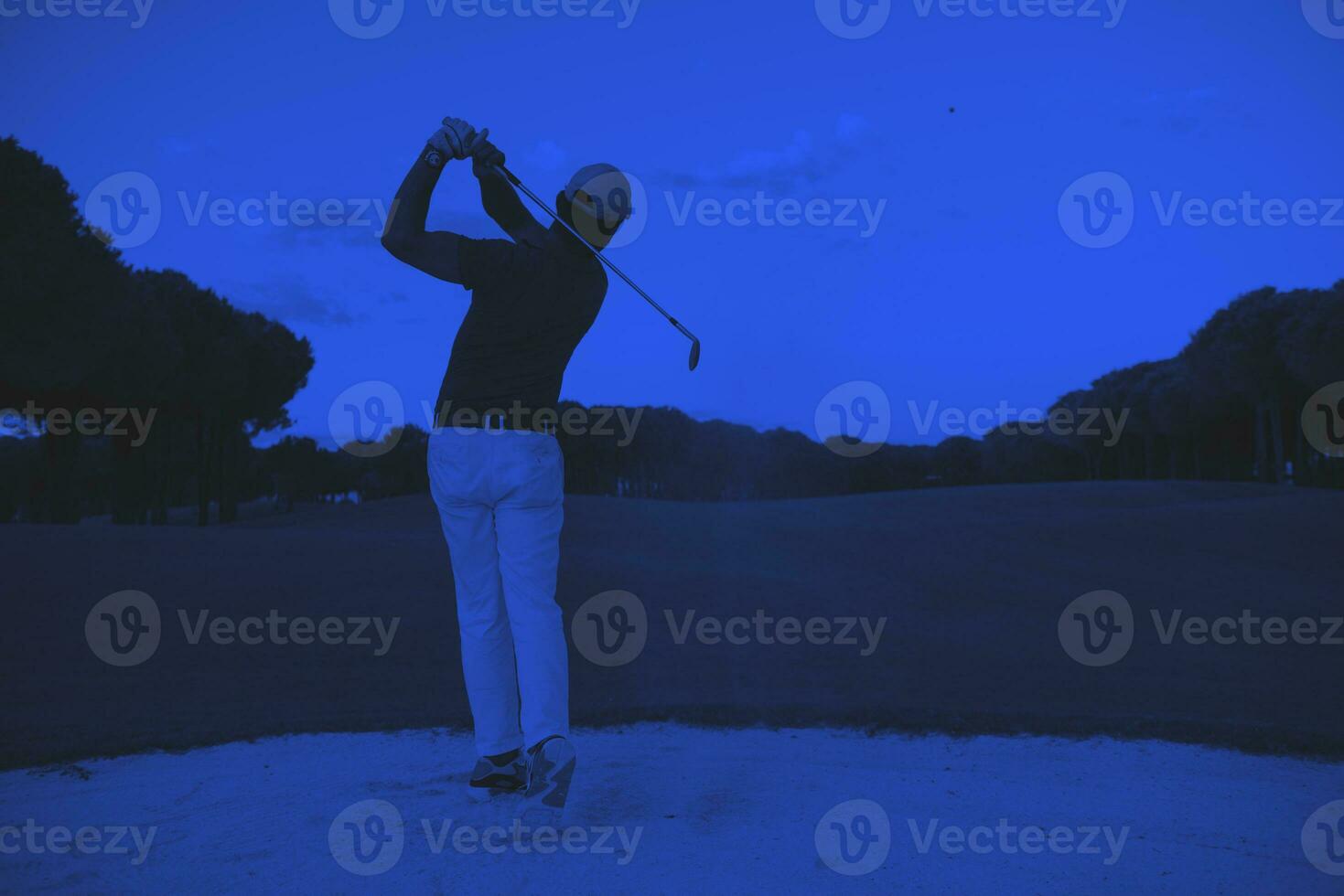 golfer hitting a sand bunker shot on sunset photo