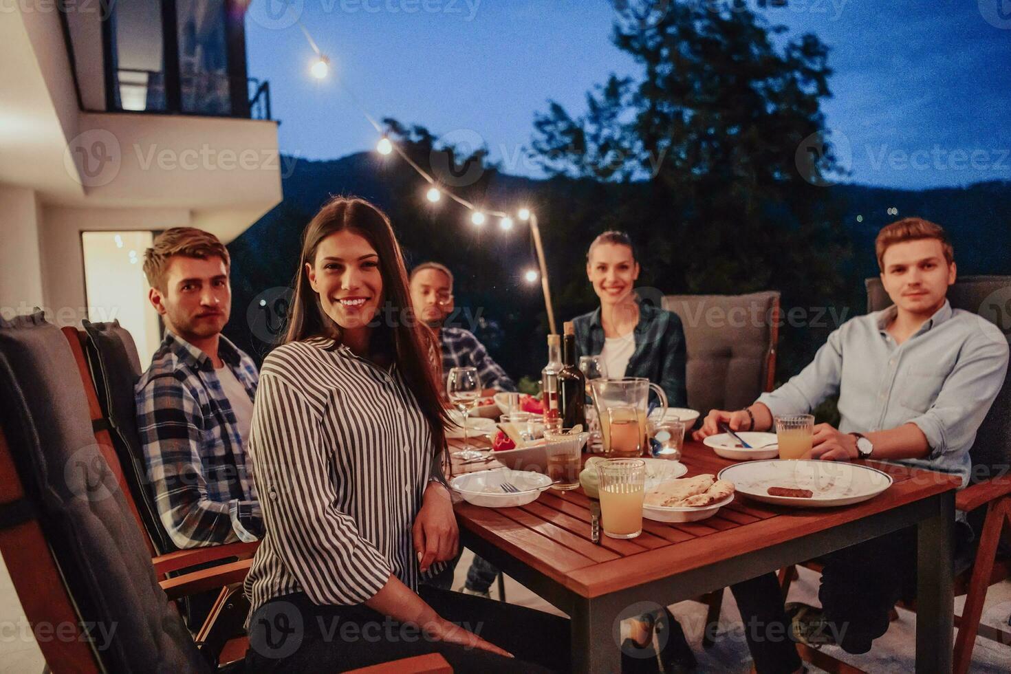 A group of young diverse people having dinner on the terrace of a modern house in the evening. Fun for friends and family. Celebration of holidays, weddings with barbecue. photo