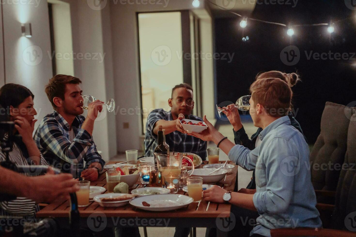 A group of young diverse people having dinner on the terrace of a modern house in the evening. Fun for friends and family. Celebration of holidays, weddings with barbecue. photo