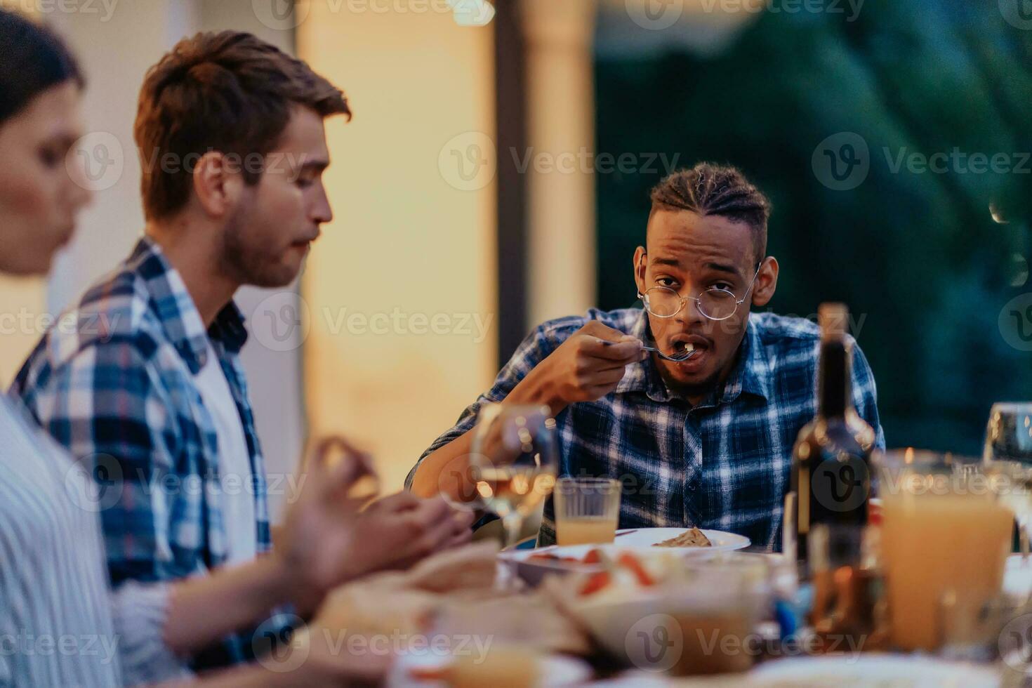 un grupo de joven diverso personas teniendo cena en el terraza de un moderno casa en el noche. divertido para amigos y familia. celebracion de vacaciones, bodas con parilla. foto