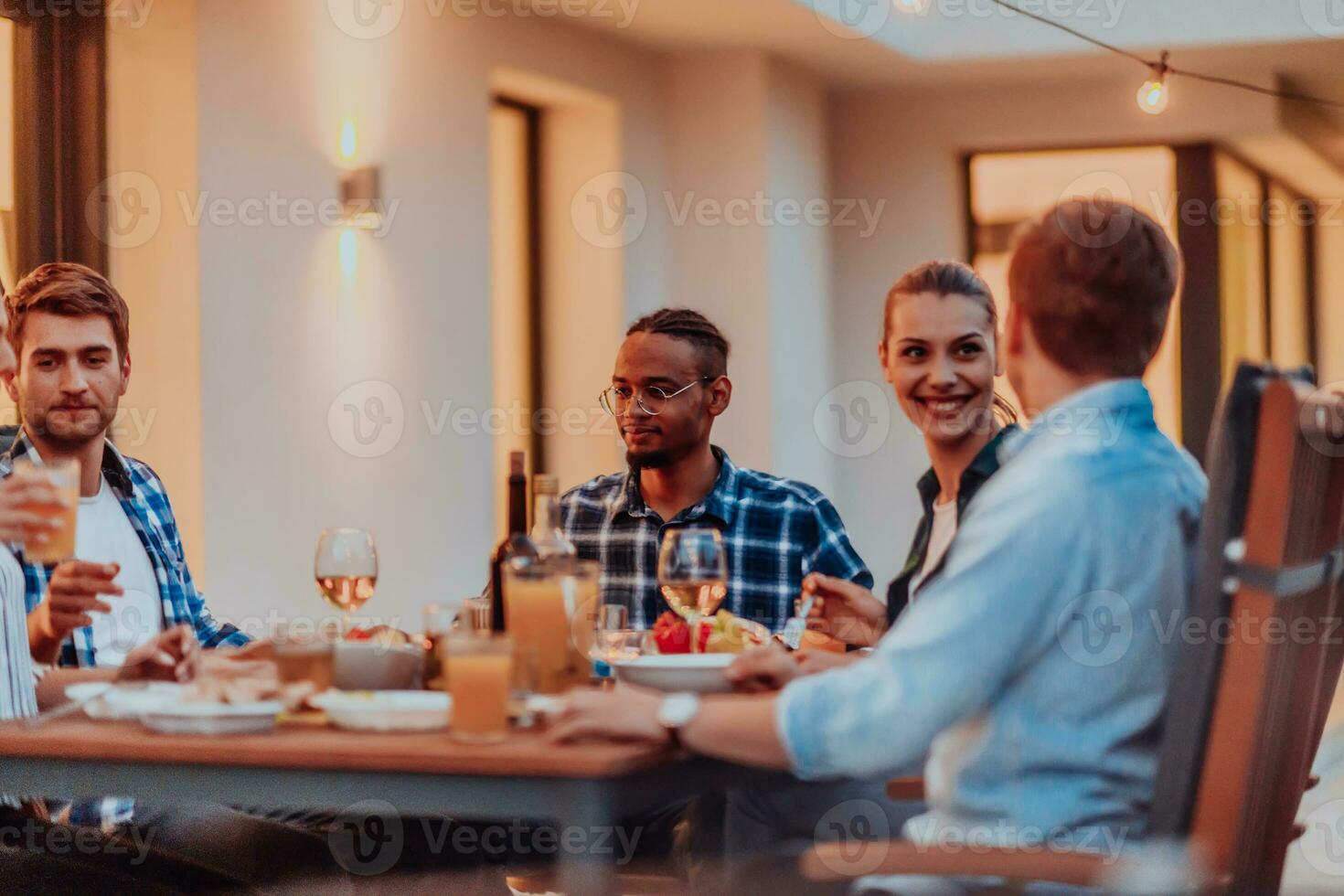 A group of young diverse people having dinner on the terrace of a modern house in the evening. Fun for friends and family. Celebration of holidays, weddings with barbecue. photo