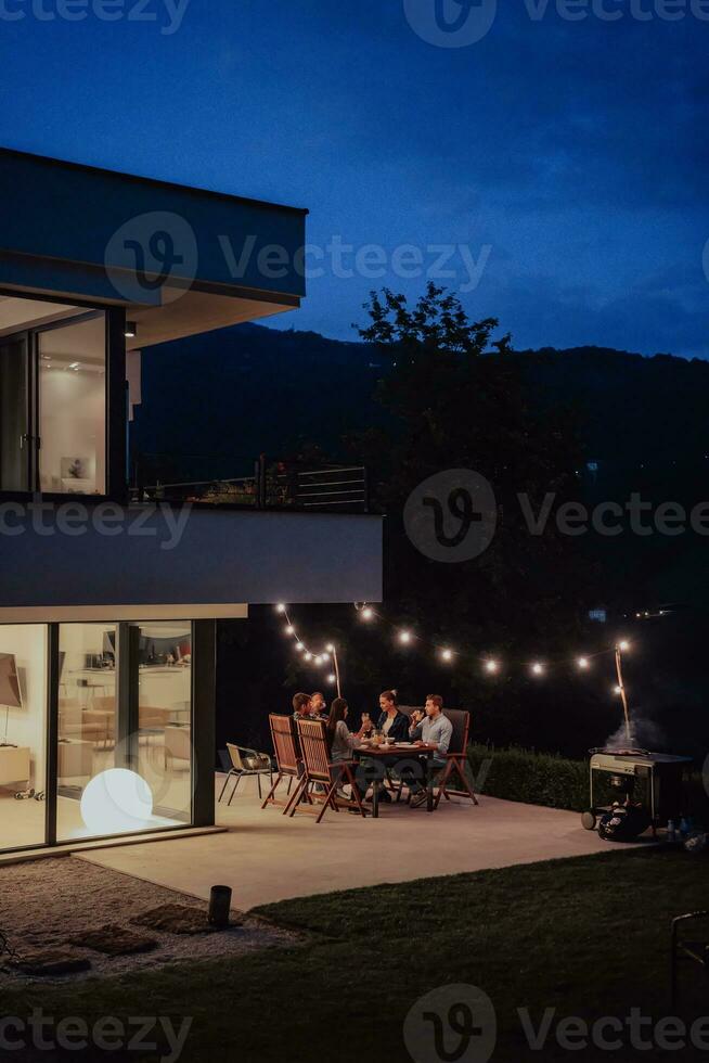 A group of young diverse people having dinner on the terrace of a modern house in the evening. Fun for friends and family. Celebration of holidays, weddings with barbecue. photo