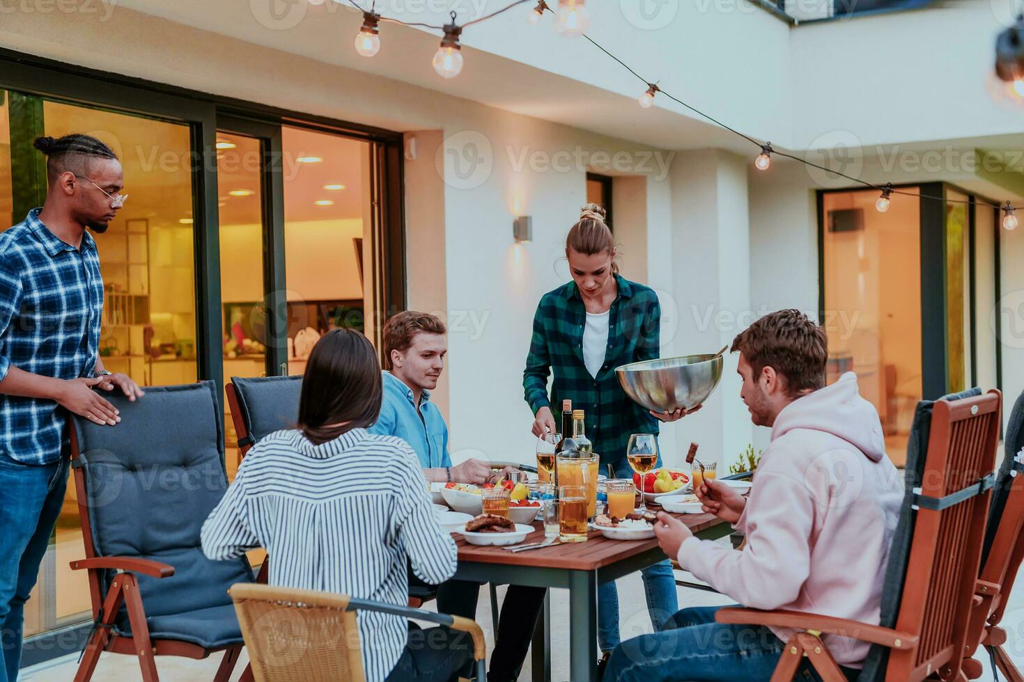 A group of young diverse people having dinner on the terrace of a modern house in the evening. Fun for friends and family. Celebration of holidays, weddings with barbecue. photo