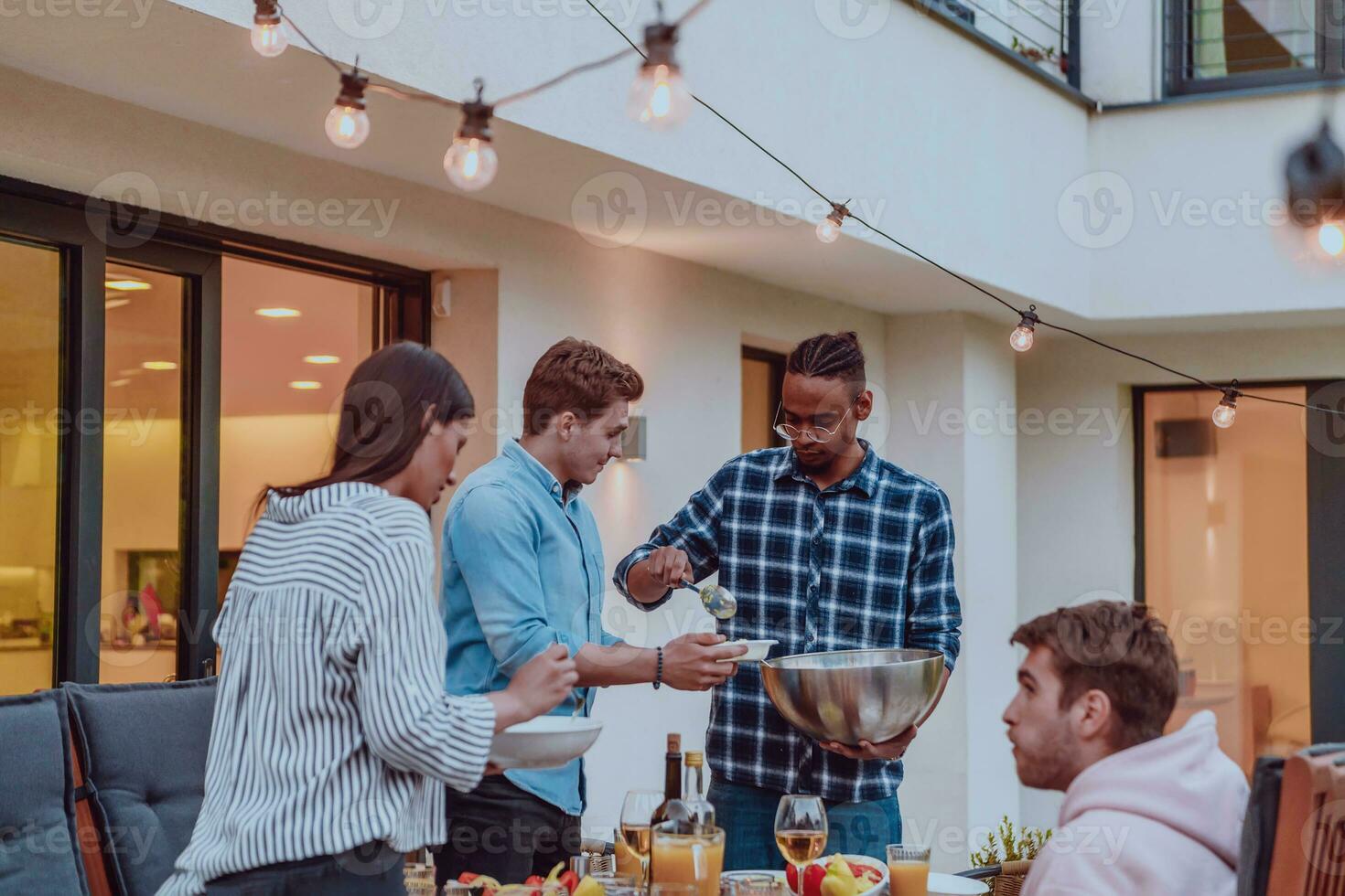 A group of friends and family barbecue together in the evening on the terrace in front of a large modern house photo