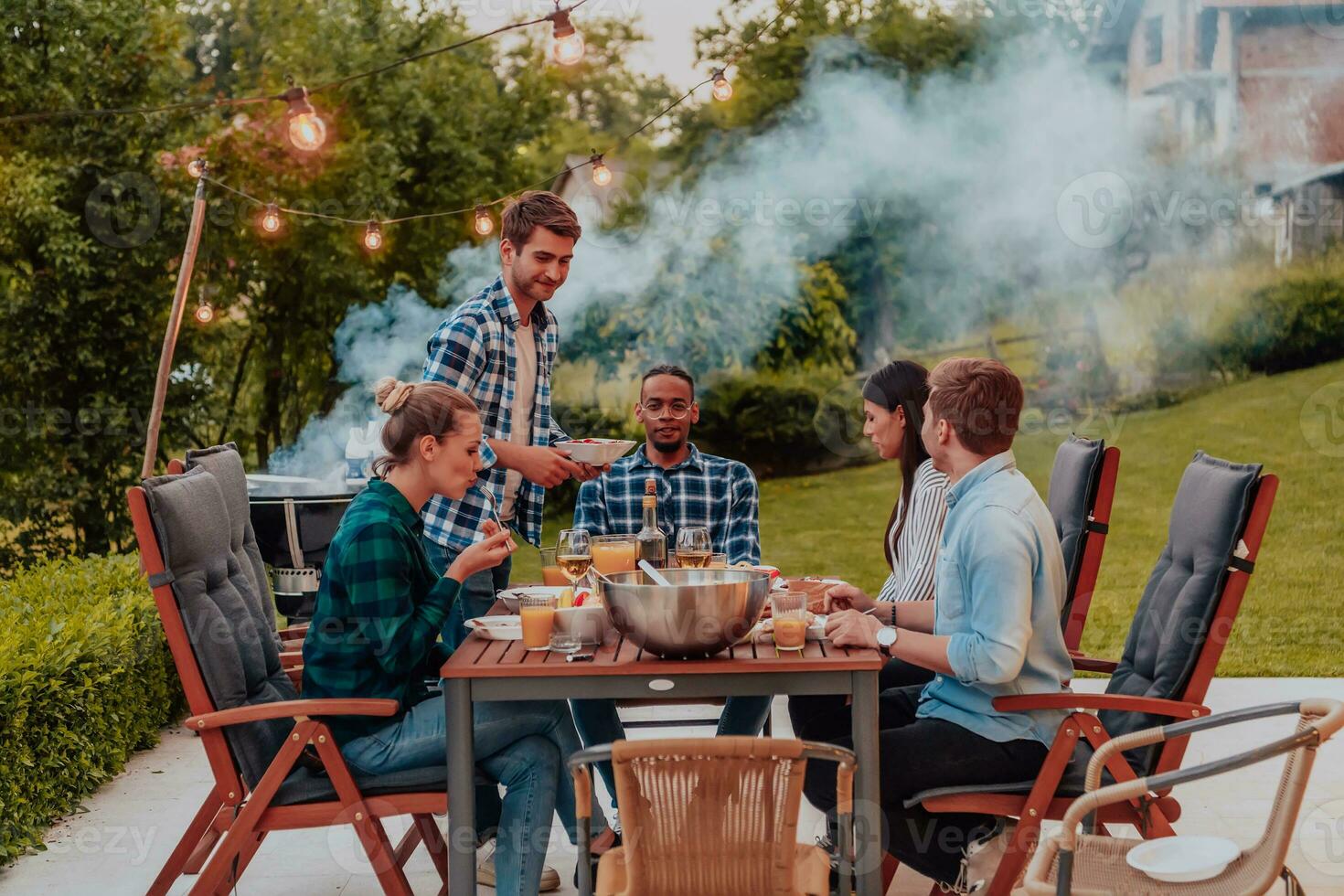 A group of young diverse people having dinner on the terrace of a modern house in the evening. Fun for friends and family. Celebration of holidays, weddings with barbecue. photo