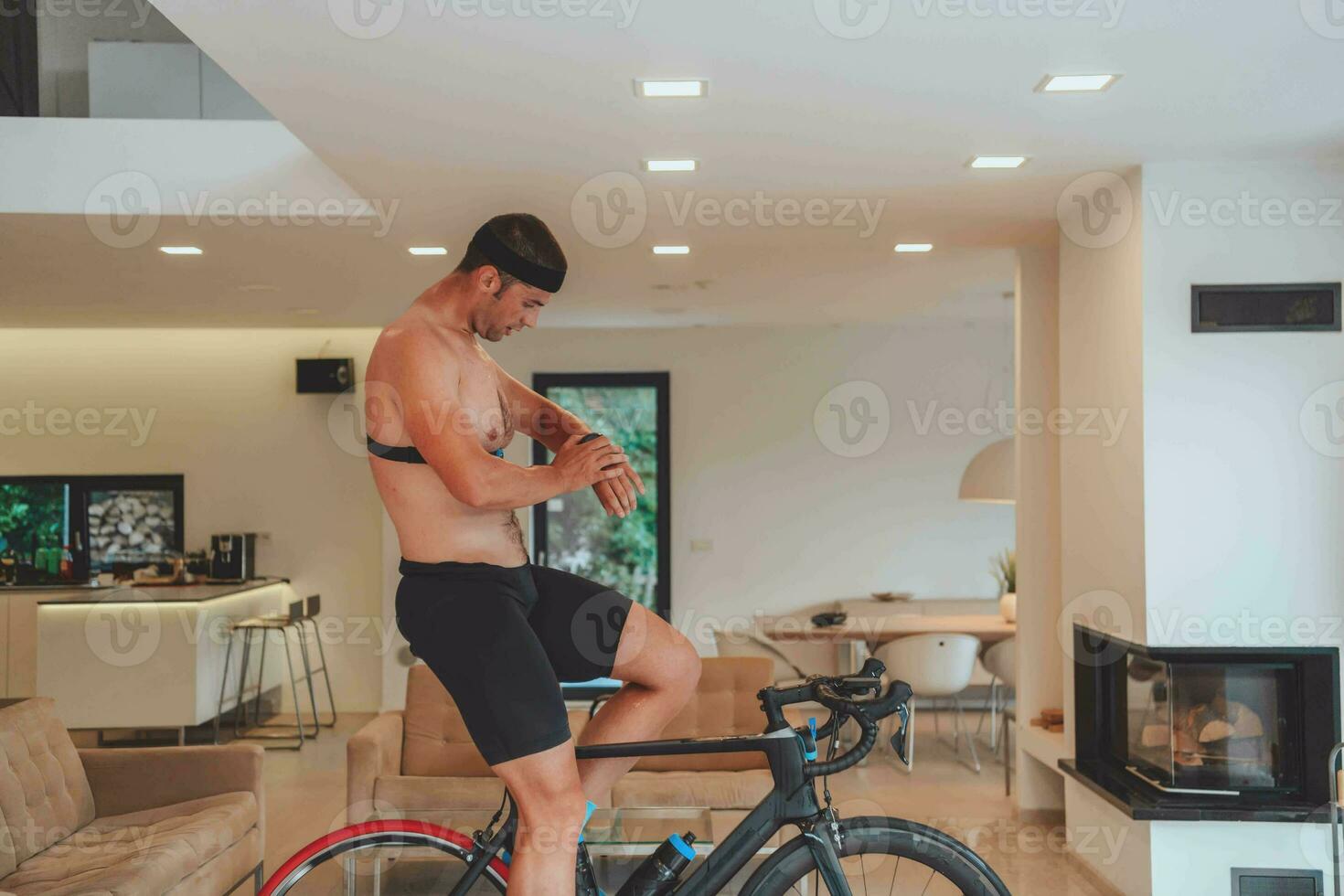 un hombre montando un triatlón bicicleta en un máquina simulación en un moderno vivo habitación. formación durante pandemia condiciones. foto