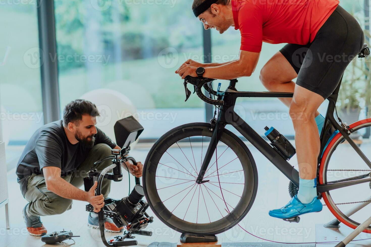 A cameraman filming an athlete riding a triathlon bike on a simulation machine in a modern living room. Training in pandemic conditions. photo