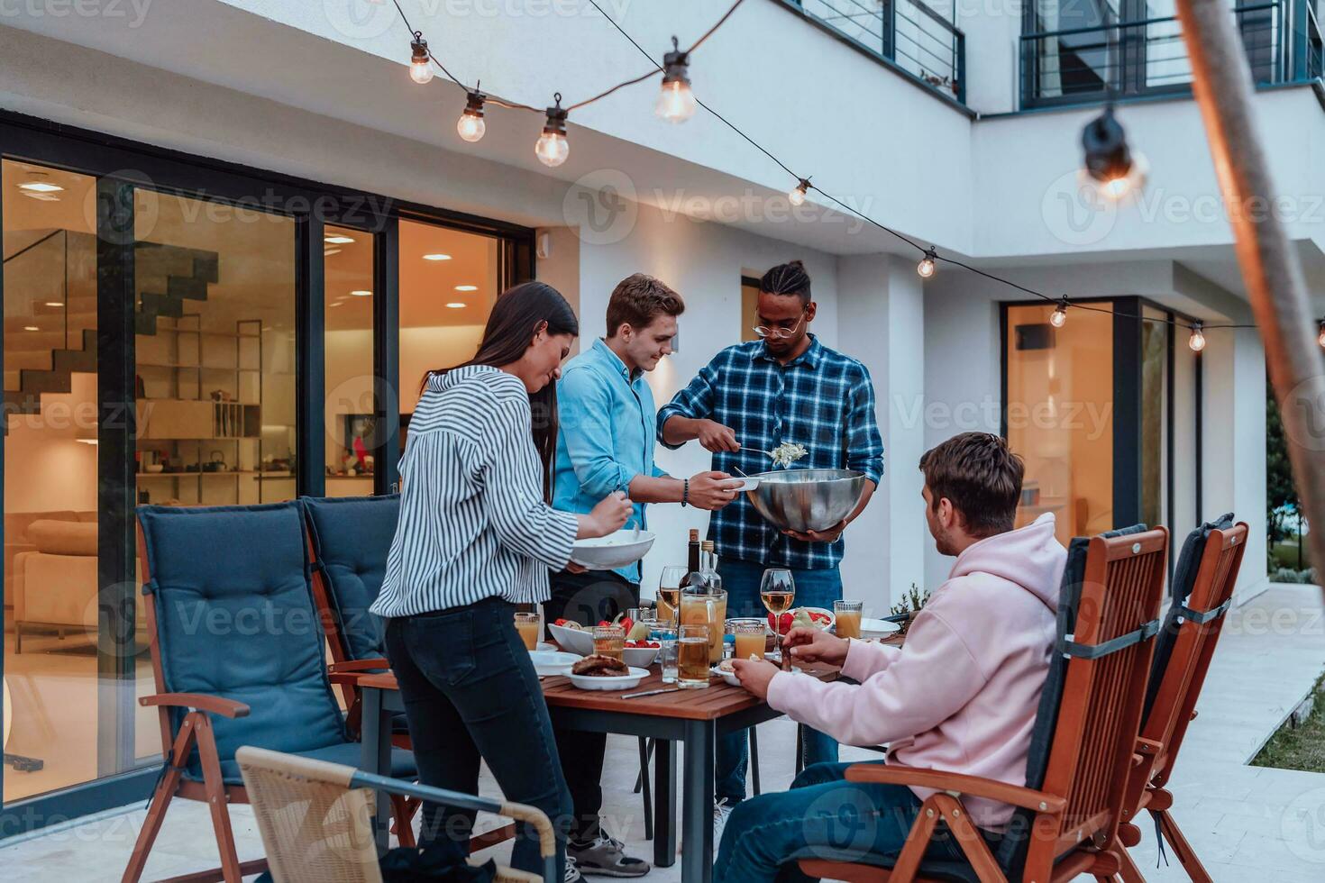 A group of young diverse people having dinner on the terrace of a modern house in the evening. Fun for friends and family. Celebration of holidays, weddings with barbecue. photo