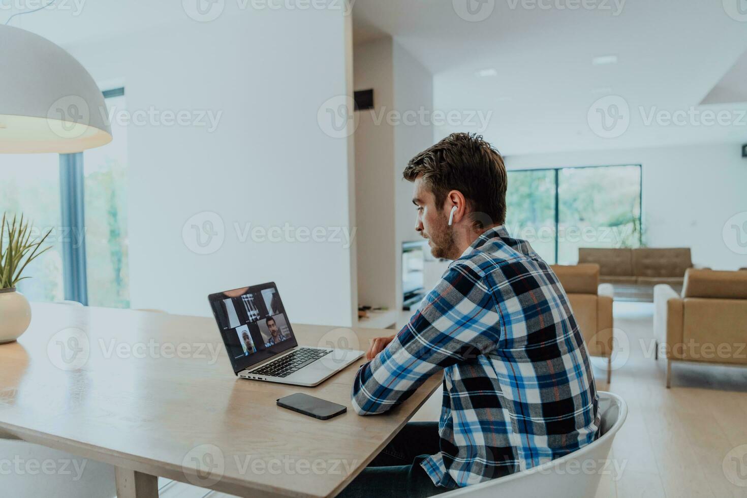 The man sitting at a table in a modern living room, with headphones using a laptop for business video chat, conversation with friends and entertainment photo