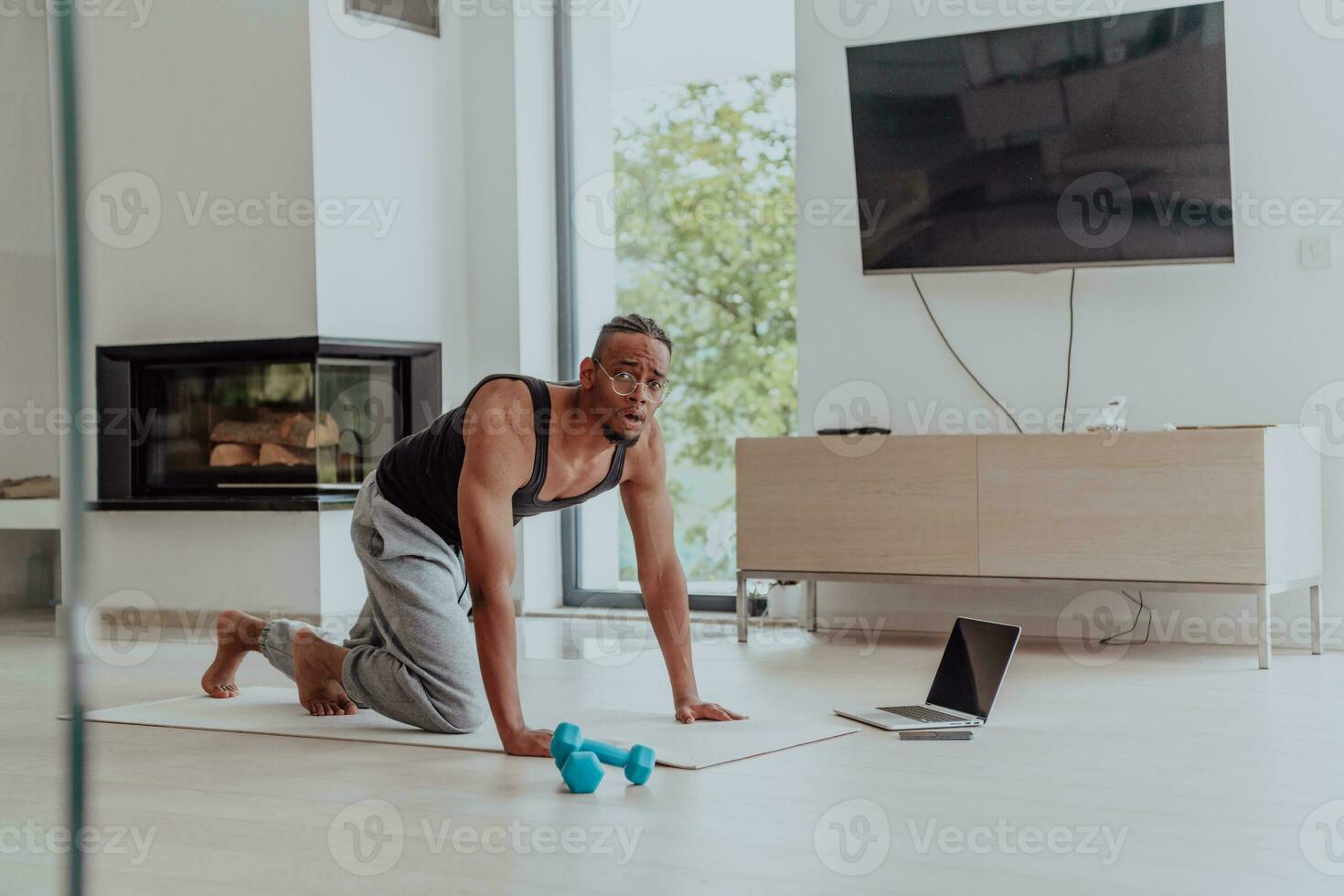 Training At Home. Sporty man doing training while watching online tutorial on laptop, exercising in living room, free space photo