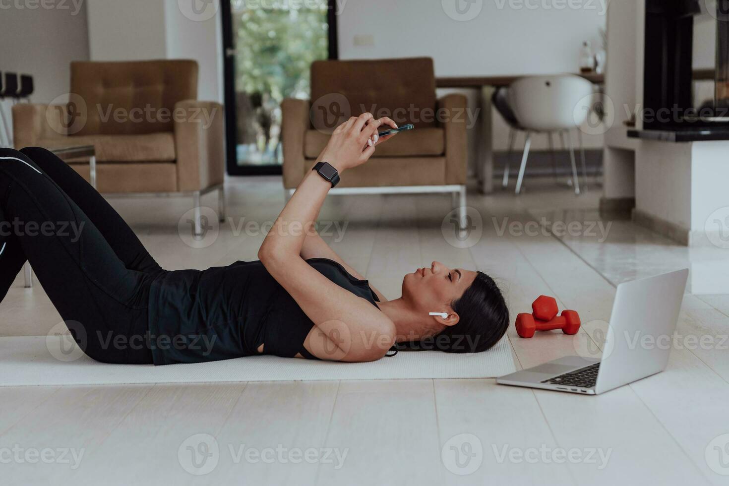 Sportswoman using a smartphone while resting and lying on floor of modern house photo