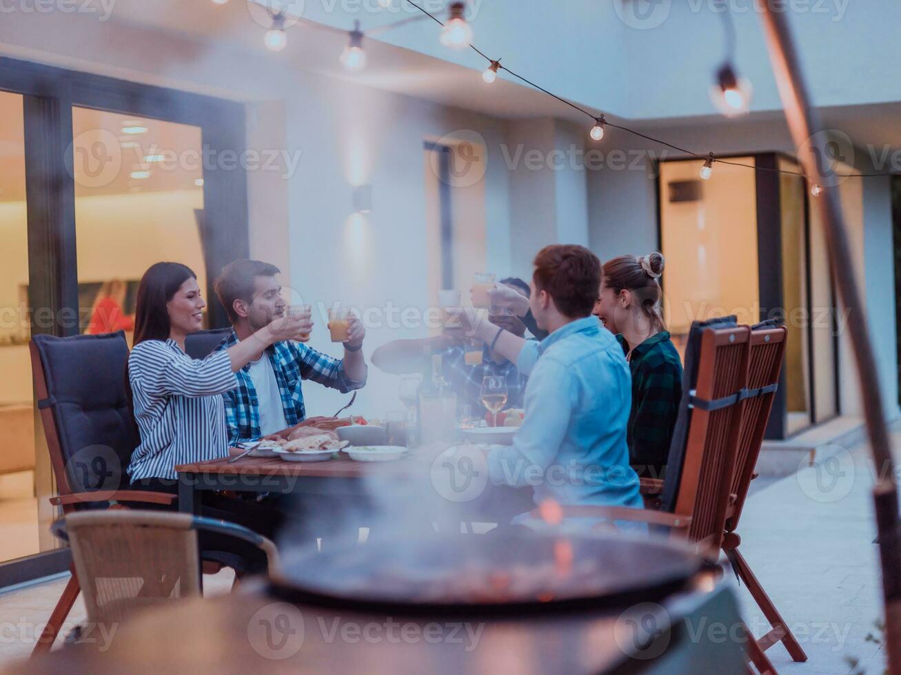 A group of young diverse people having dinner on the terrace of a modern house in the evening. Fun for friends and family. Celebration of holidays, weddings with barbecue. photo