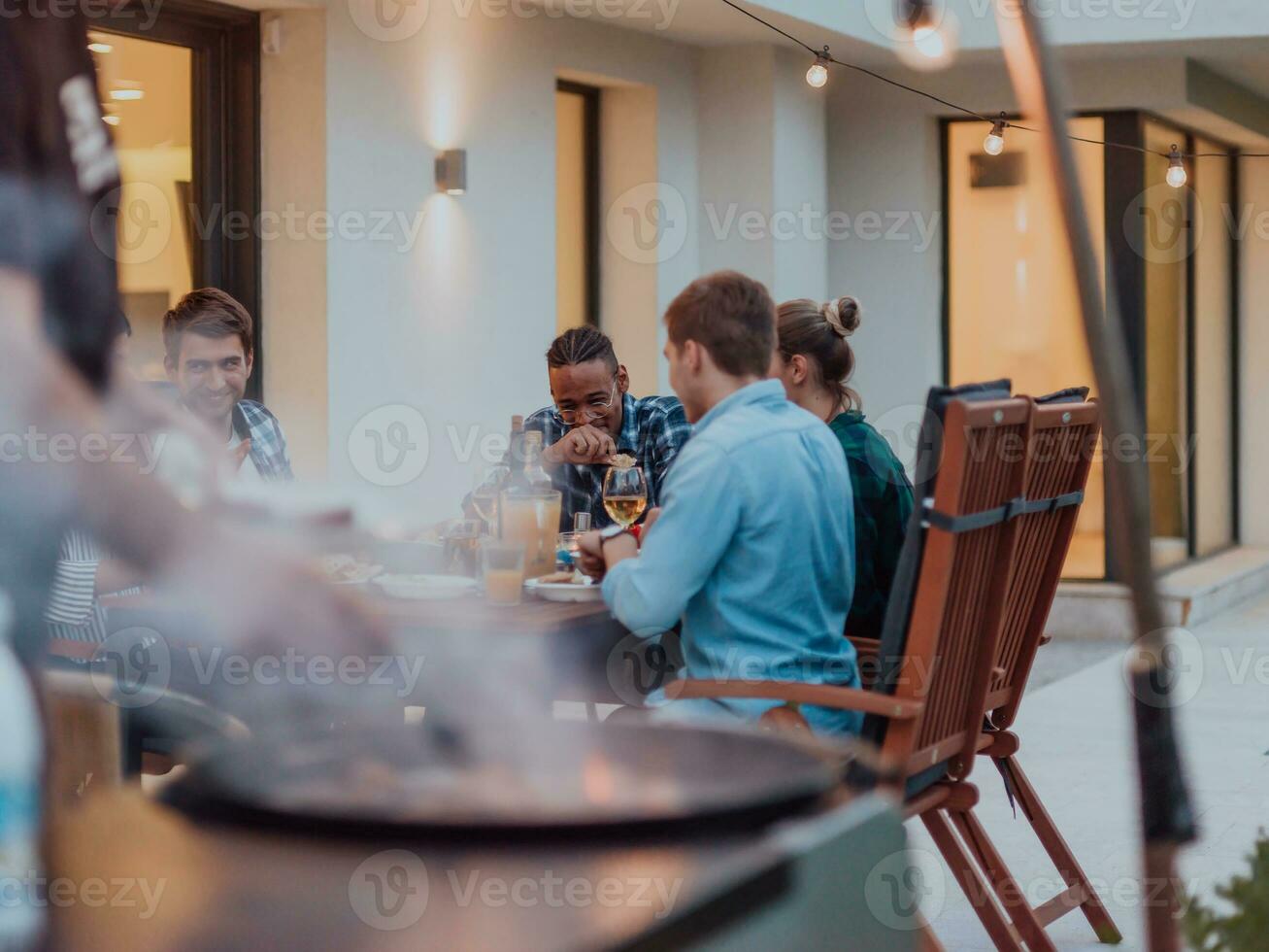 A group of young diverse people having dinner on the terrace of a modern house in the evening. Fun for friends and family. Celebration of holidays, weddings with barbecue. photo