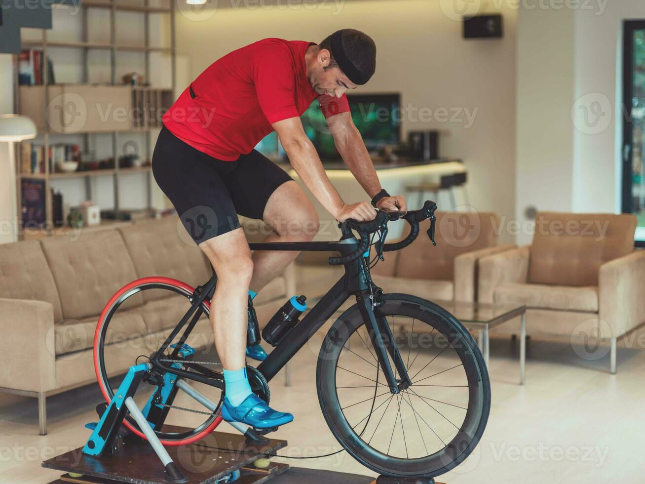 A man riding a triathlon bike on a machine simulation in a modern living room. Training during pandemic conditions. photo