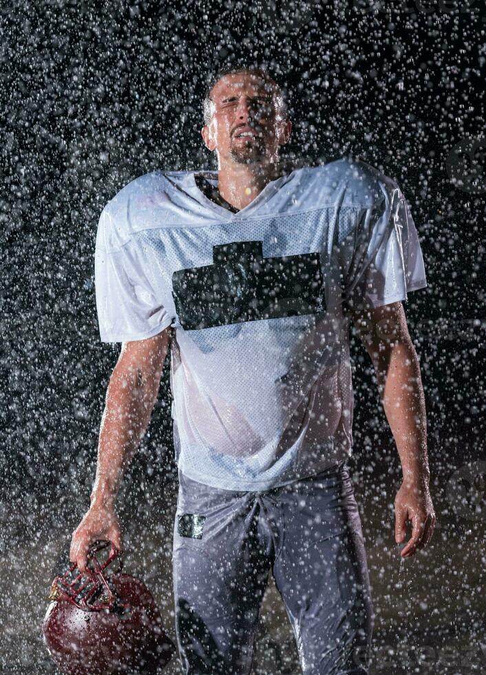 American Football Field Lonely Athlete Warrior Standing on a Field Holds his Helmet and Ready to Play. Player Preparing to Run, Attack and Score Touchdown. Rainy Night with Dramatic Fog, Blue Light photo