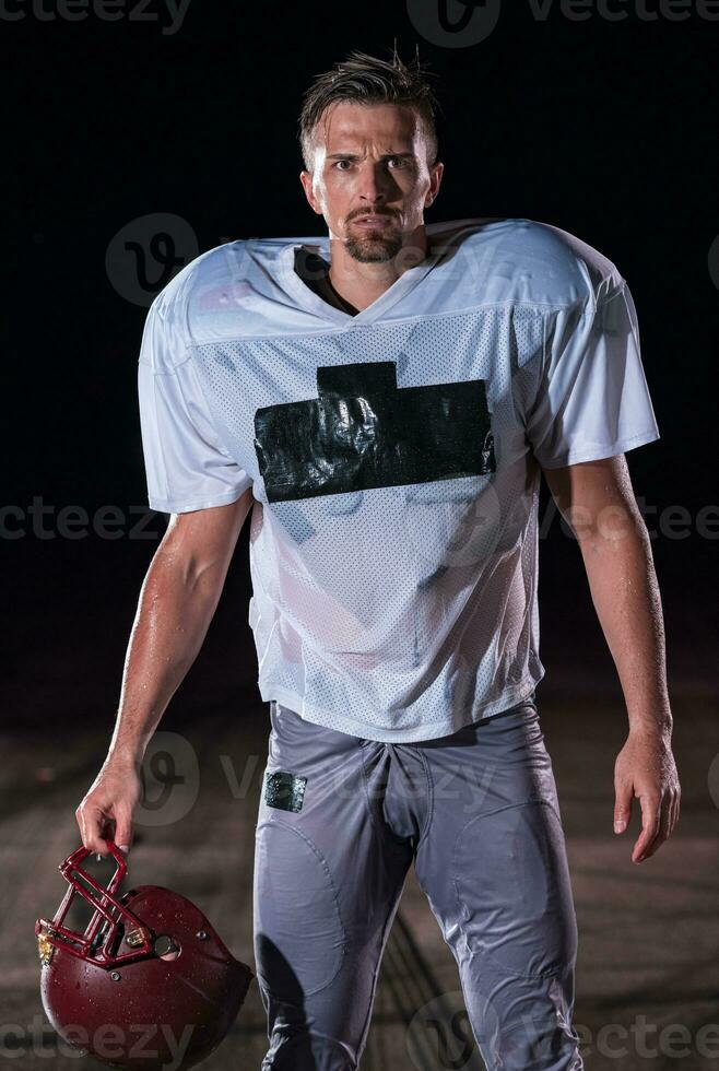 American Football Field Lonely Athlete Warrior Standing on a Field Holds his Helmet and Ready to Play. Player Preparing to Run, Attack and Score Touchdown. Rainy Night with Dramatic Fog, Blue Light photo