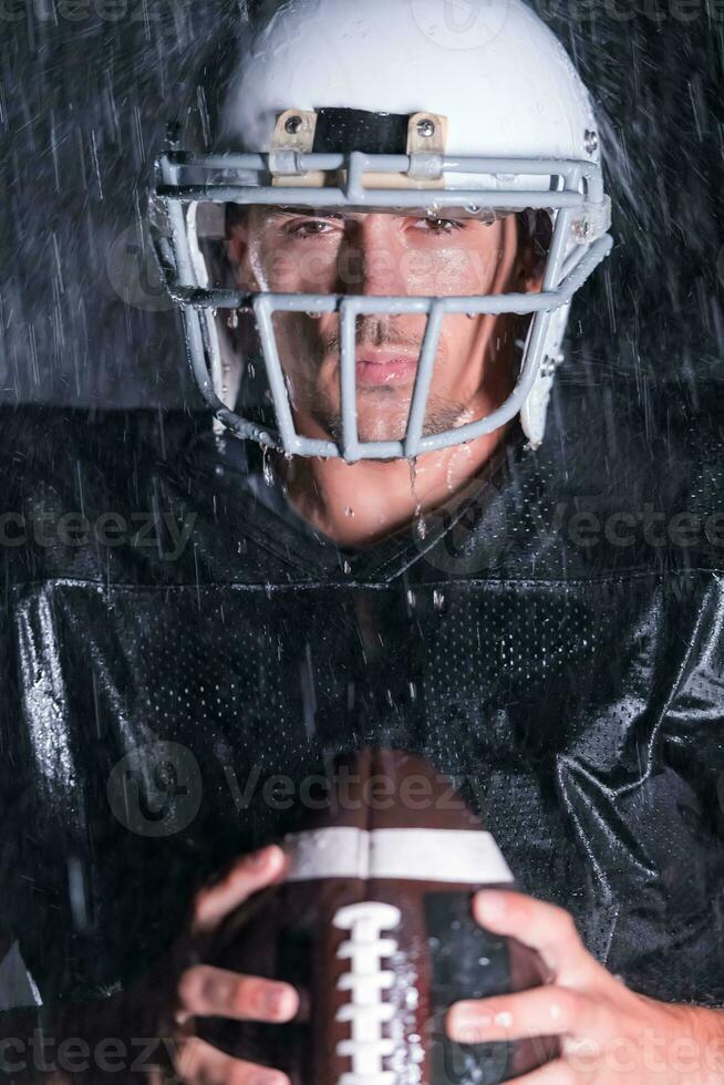 American Football Field Lonely Athlete Warrior Standing on a Field Holds his Helmet and Ready to Play. Player Preparing to Run, Attack and Score Touchdown. Rainy Night with Dramatic Fog, Blue Light photo