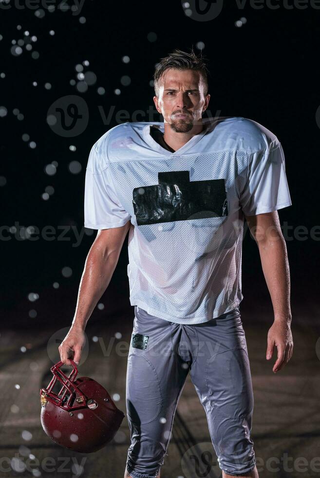 American Football Field Lonely Athlete Warrior Standing on a Field Holds his Helmet and Ready to Play. Player Preparing to Run, Attack and Score Touchdown. Rainy Night with Dramatic Fog, Blue Light photo