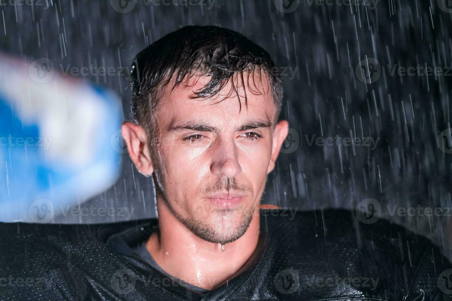 American Football Field Lonely Athlete Warrior Standing on a Field Holds his Helmet and Ready to Play. Player Preparing to Run, Attack and Score Touchdown. Rainy Night with Dramatic Fog, Blue Light photo