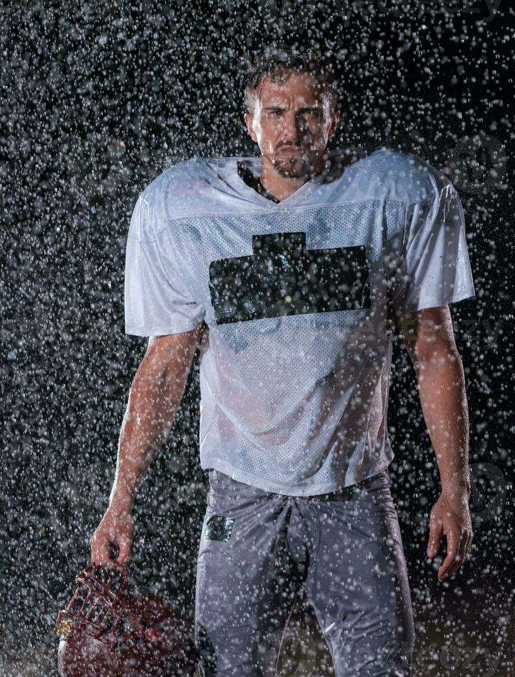 American Football Field Lonely Athlete Warrior Standing on a Field Holds his Helmet and Ready to Play. Player Preparing to Run, Attack and Score Touchdown. Rainy Night with Dramatic Fog, Blue Light photo