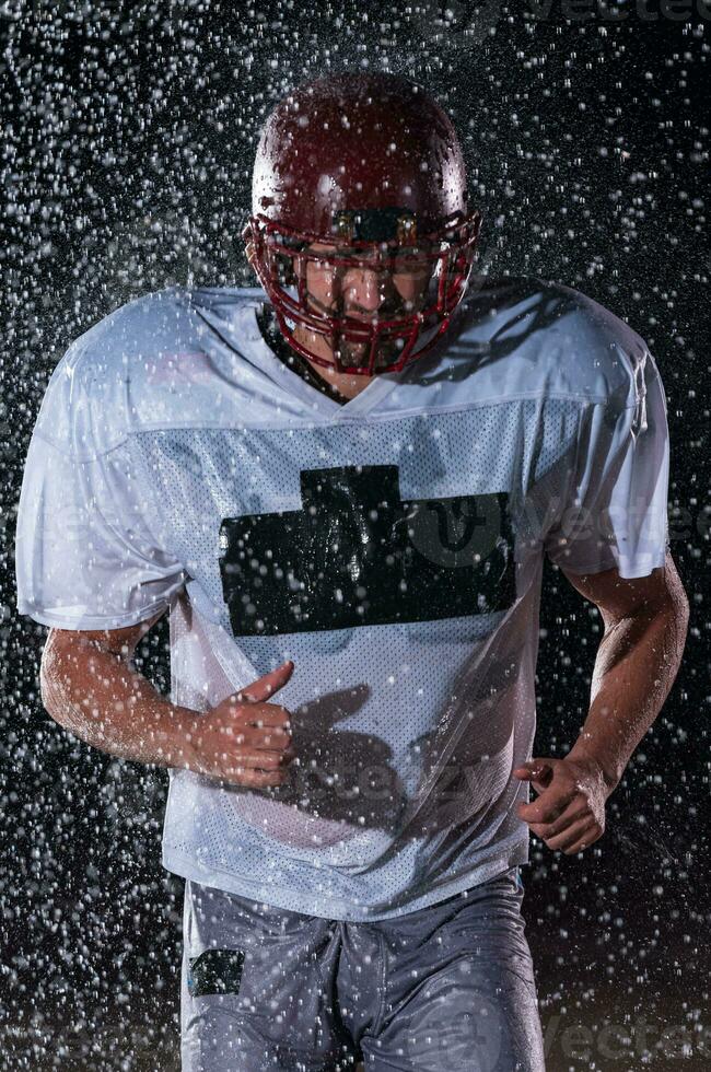 American Football Field Lonely Athlete Warrior Standing on a Field Holds his Helmet and Ready to Play. Player Preparing to Run, Attack and Score Touchdown. Rainy Night with Dramatic Fog, Blue Light photo