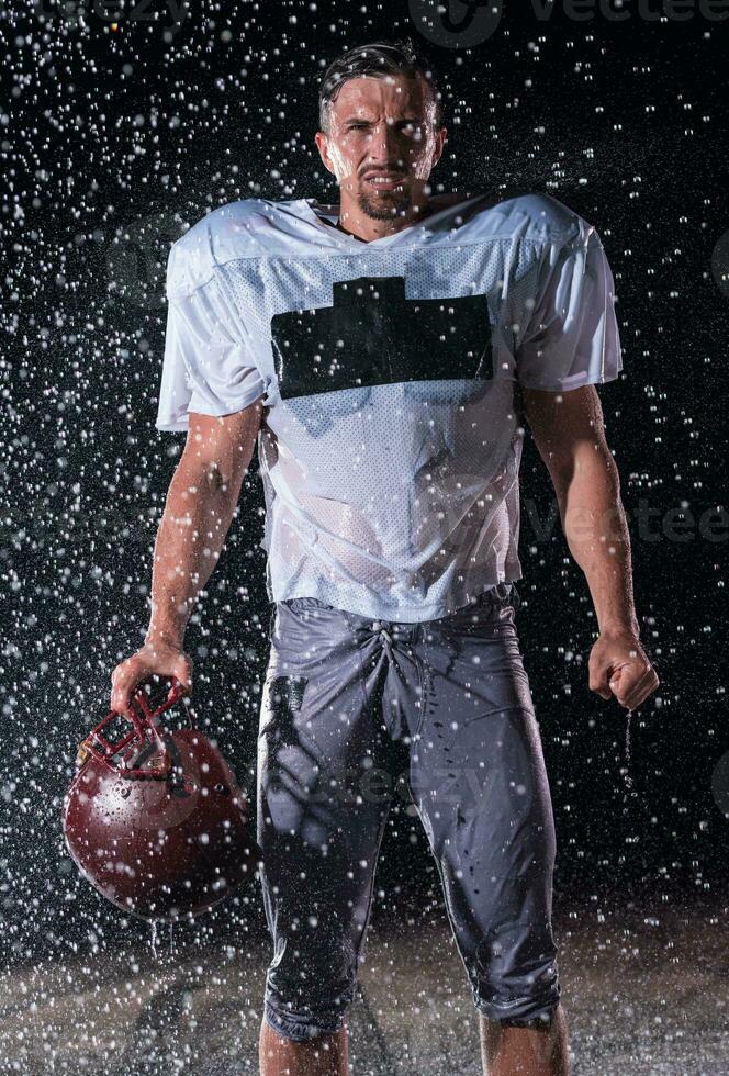 American Football Field Lonely Athlete Warrior Standing on a Field Holds his Helmet and Ready to Play. Player Preparing to Run, Attack and Score Touchdown. Rainy Night with Dramatic Fog, Blue Light photo