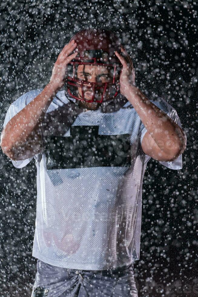 American Football Field Lonely Athlete Warrior Standing on a Field Holds his Helmet and Ready to Play. Player Preparing to Run, Attack and Score Touchdown. Rainy Night with Dramatic Fog, Blue Light photo