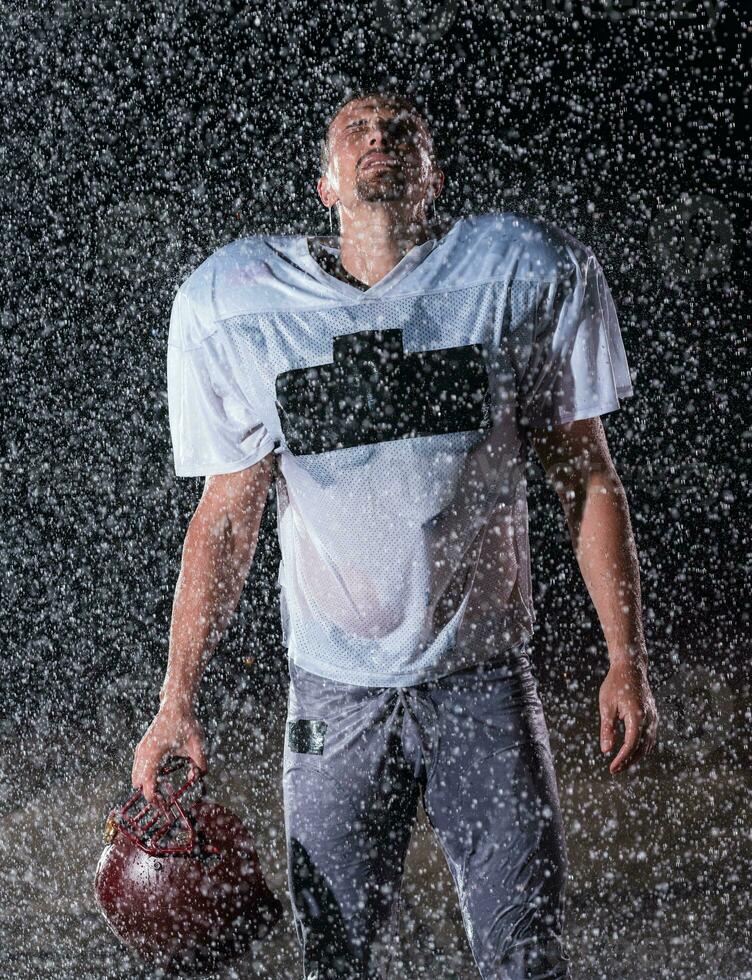 American Football Field Lonely Athlete Warrior Standing on a Field Holds his Helmet and Ready to Play. Player Preparing to Run, Attack and Score Touchdown. Rainy Night with Dramatic Fog, Blue Light photo
