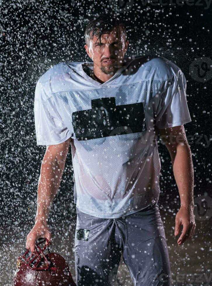 American Football Field Lonely Athlete Warrior Standing on a Field Holds his Helmet and Ready to Play. Player Preparing to Run, Attack and Score Touchdown. Rainy Night with Dramatic Fog, Blue Light photo