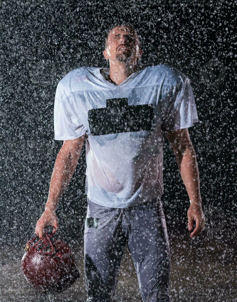 American Football Field Lonely Athlete Warrior Standing on a Field Holds his Helmet and Ready to Play. Player Preparing to Run, Attack and Score Touchdown. Rainy Night with Dramatic Fog, Blue Light photo