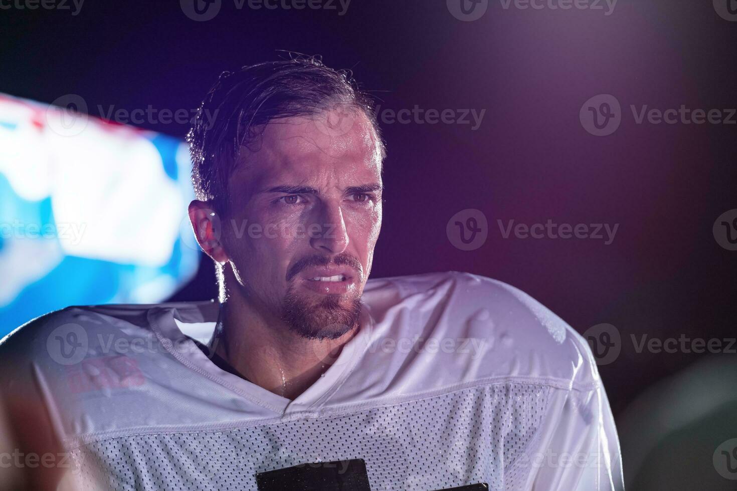 American Football Field Lonely Athlete Warrior Standing on a Field Holds his Helmet and Ready to Play. Player Preparing to Run, Attack and Score Touchdown. Rainy Night with Dramatic Fog, Blue Light photo