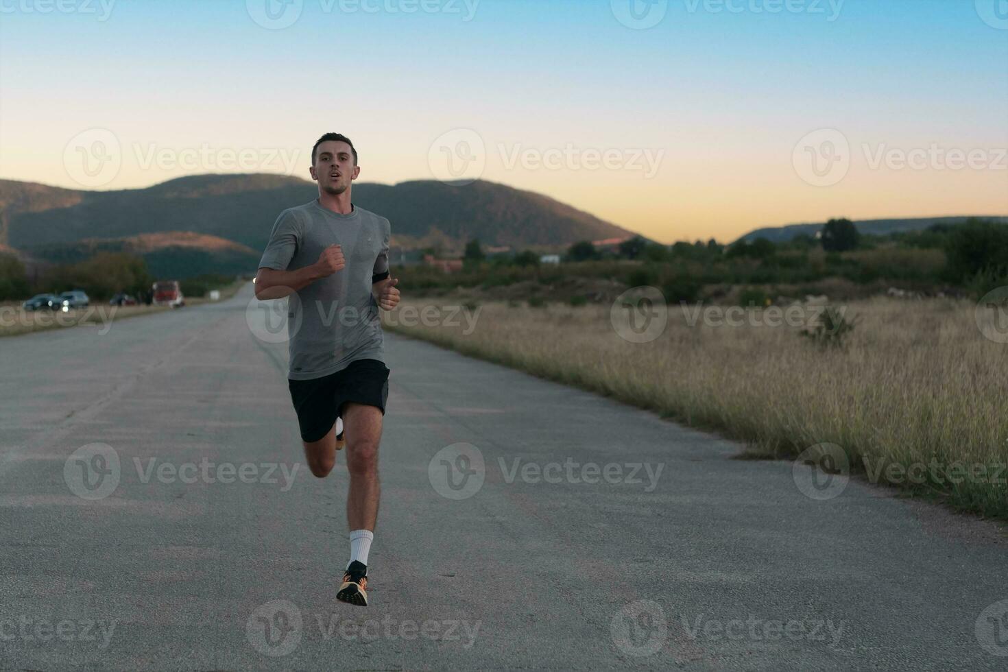 Attractive fit man running fast along countryside road at sunset light, doing jogging workout outdoors photo