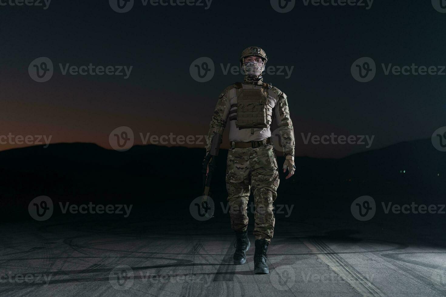 Army soldier in Combat Uniforms with an assault rifle, plate carrier and combat helmet going on a dangerous mission on a rainy night. photo