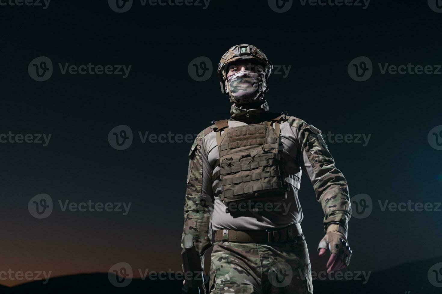 Army soldier in Combat Uniforms with an assault rifle, plate carrier and combat helmet going on a dangerous mission on a rainy night. photo