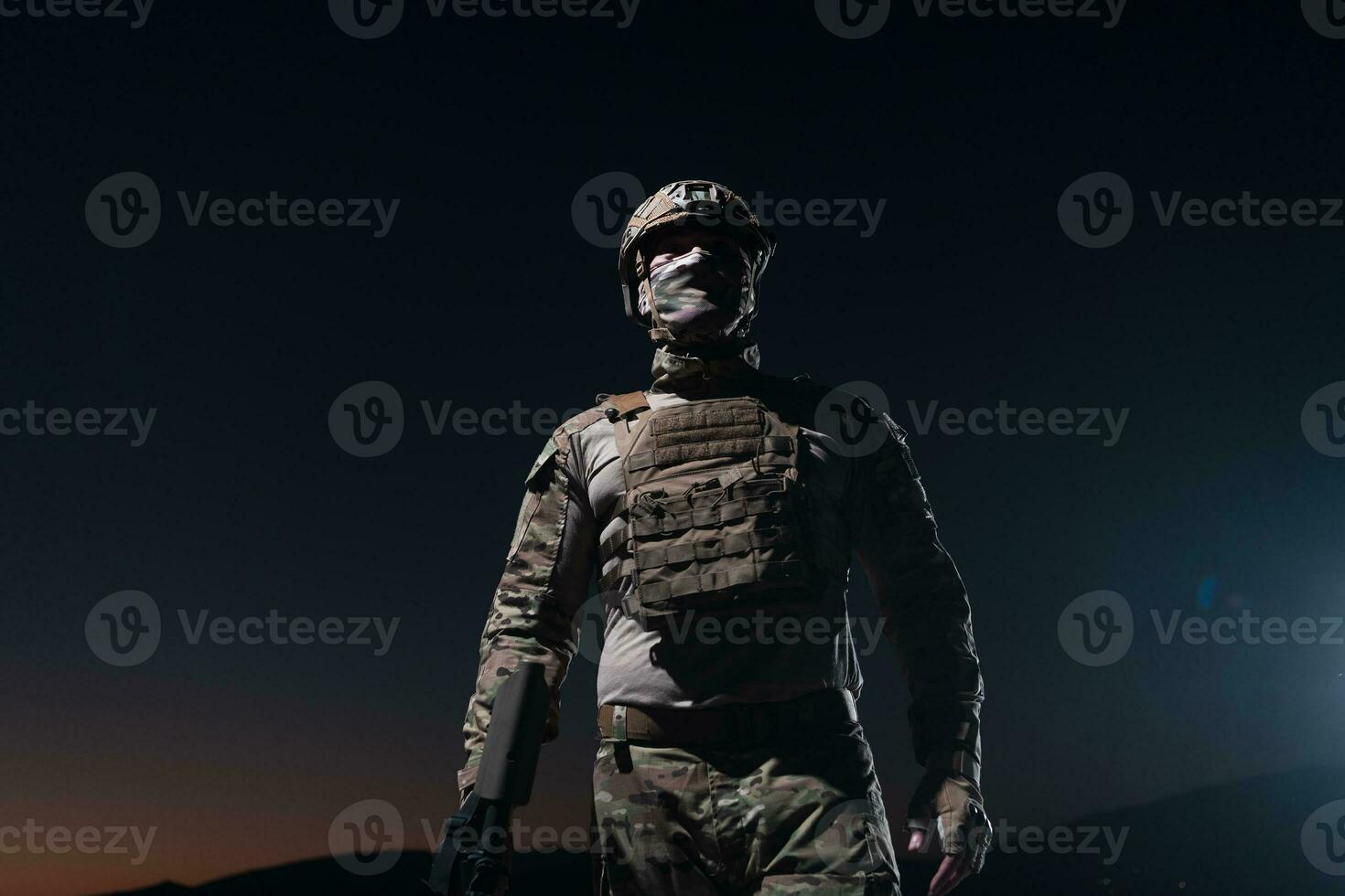 Army soldier in Combat Uniforms with an assault rifle, plate carrier and combat helmet going on a dangerous mission on a rainy night. photo