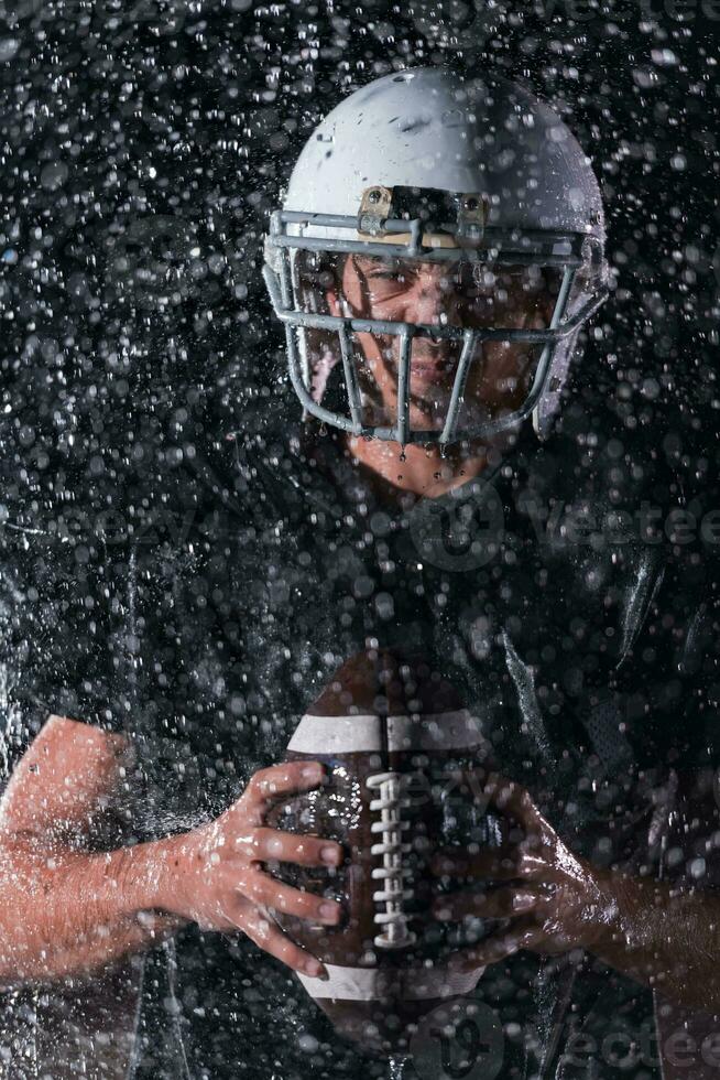 American Football Field Lonely Athlete Warrior Standing on a Field Holds his Helmet and Ready to Play. Player Preparing to Run, Attack and Score Touchdown. Rainy Night with Dramatic Fog, Blue Light photo