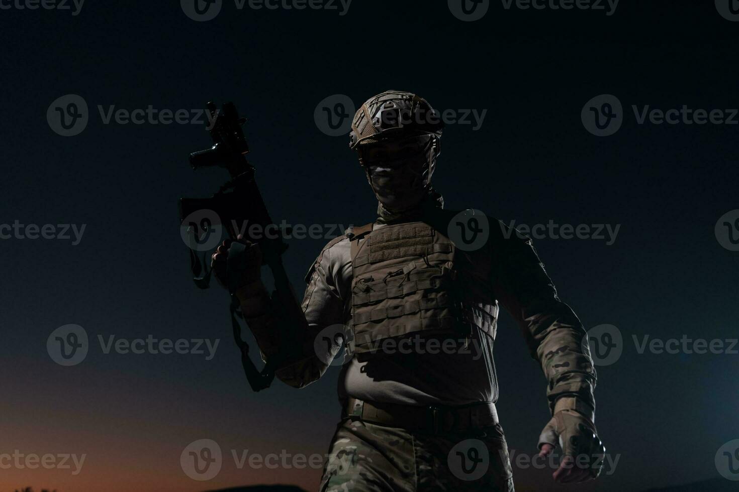 Army soldier in Combat Uniforms with an assault rifle, plate carrier and combat helmet going on a dangerous mission on a rainy night. photo