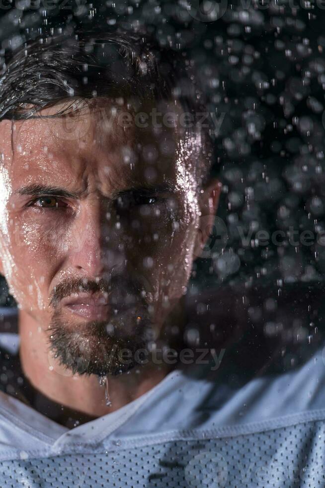 americano fútbol americano campo solitario atleta guerrero en pie en un campo sostiene su casco y Listo a jugar. jugador preparando a correr, ataque y Puntuación aterrizaje. lluvioso noche con dramático niebla, azul ligero foto