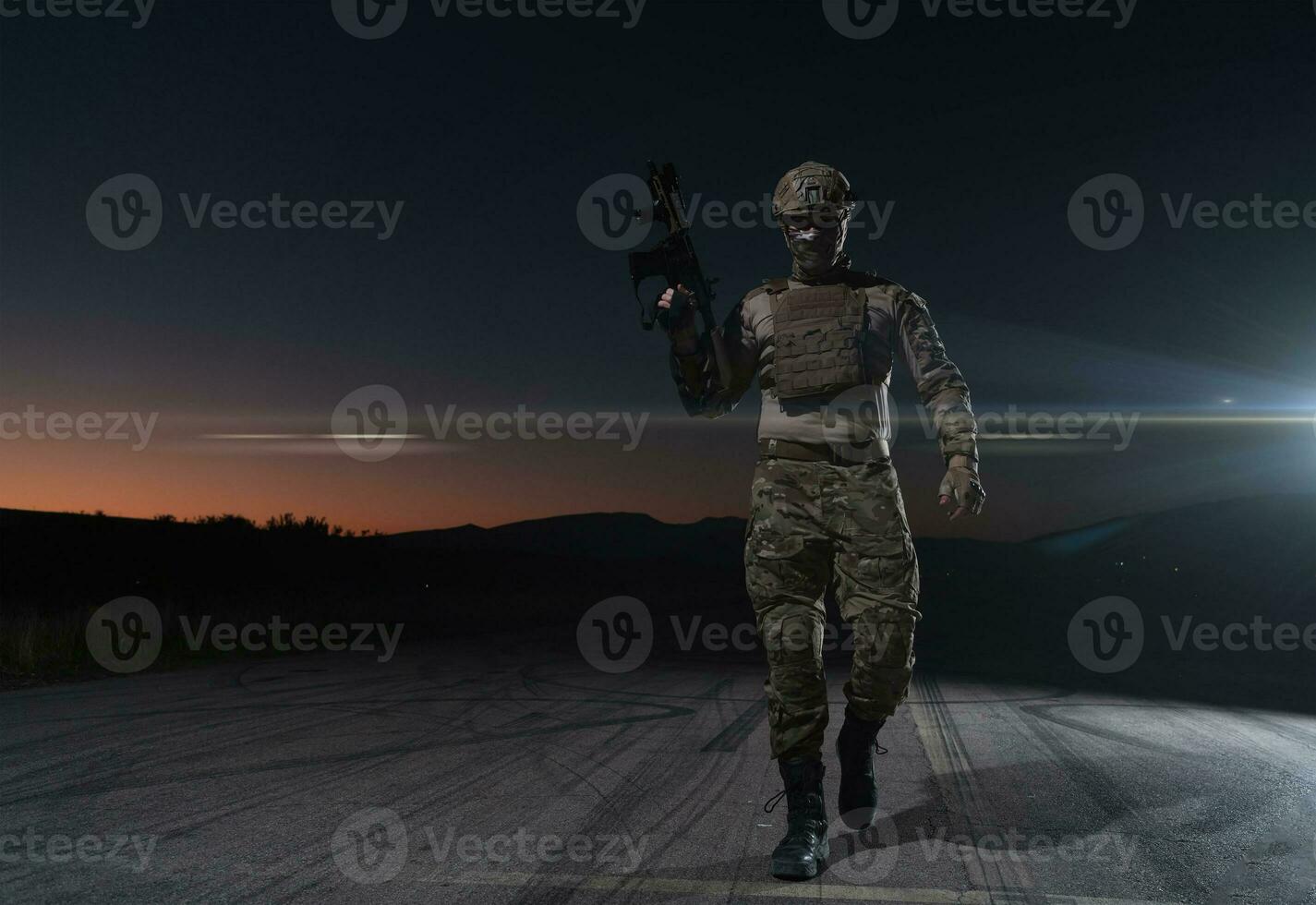 Army soldier in Combat Uniforms with an assault rifle, plate carrier and combat helmet going on a dangerous mission on a rainy night. photo