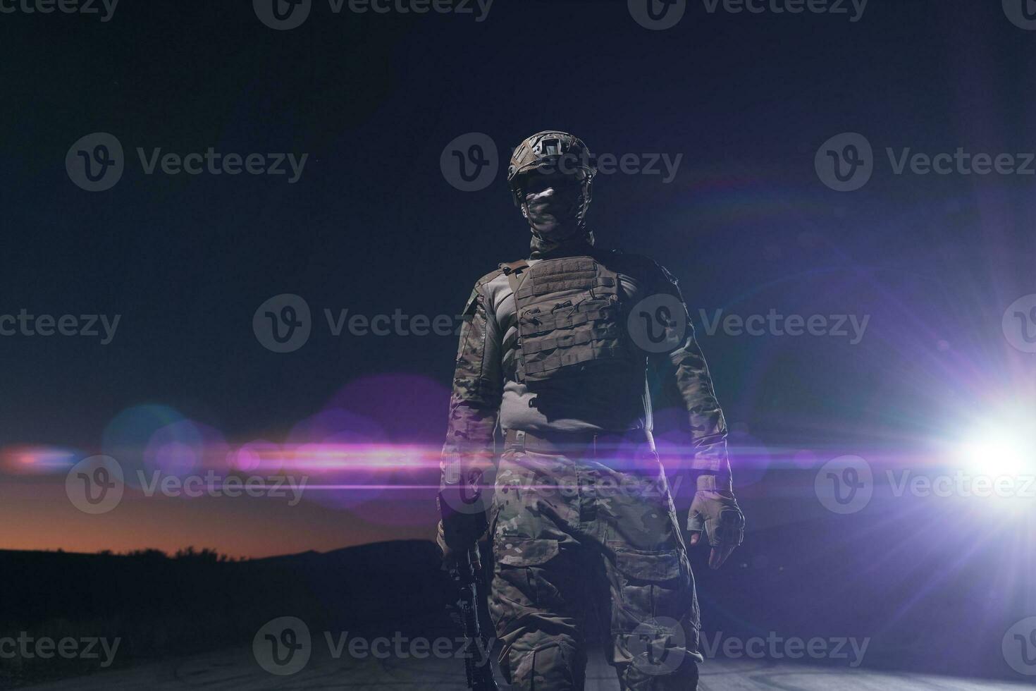 Army soldier in Combat Uniforms with an assault rifle, plate carrier and combat helmet going on a dangerous mission on a rainy night. photo