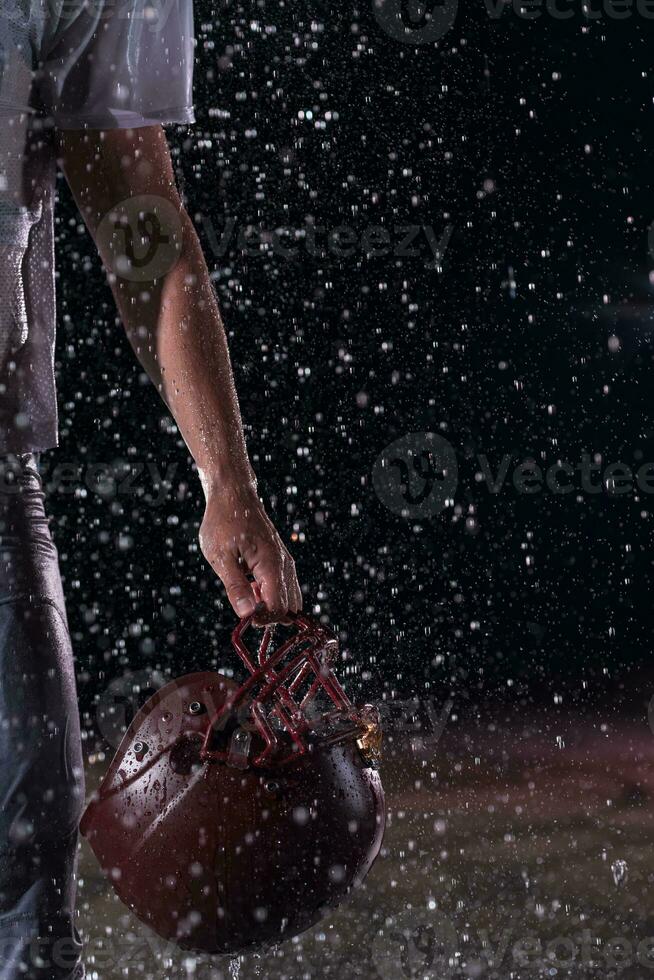 American Football Field Lonely Athlete Warrior Standing on a Field Holds his Helmet and Ready to Play. Player Preparing to Run, Attack and Score Touchdown. Rainy Night with Dramatic Fog, Blue Light photo