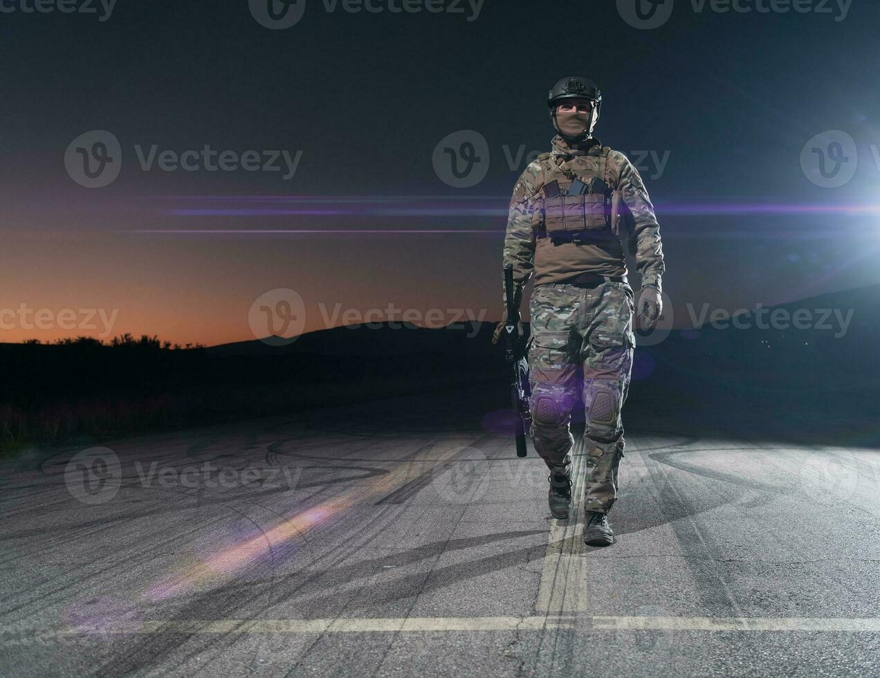 Army soldier in Combat Uniforms with an assault rifle, plate carrier and combat helmet going on a dangerous mission on a rainy night. photo