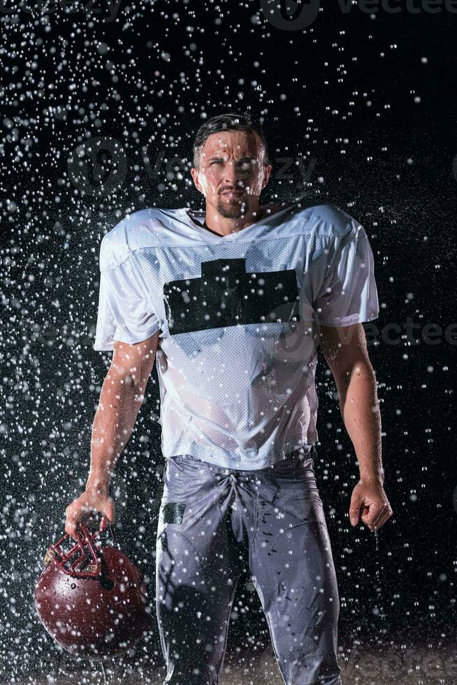 American Football Field Lonely Athlete Warrior Standing on a Field Holds his Helmet and Ready to Play. Player Preparing to Run, Attack and Score Touchdown. Rainy Night with Dramatic Fog, Blue Light photo