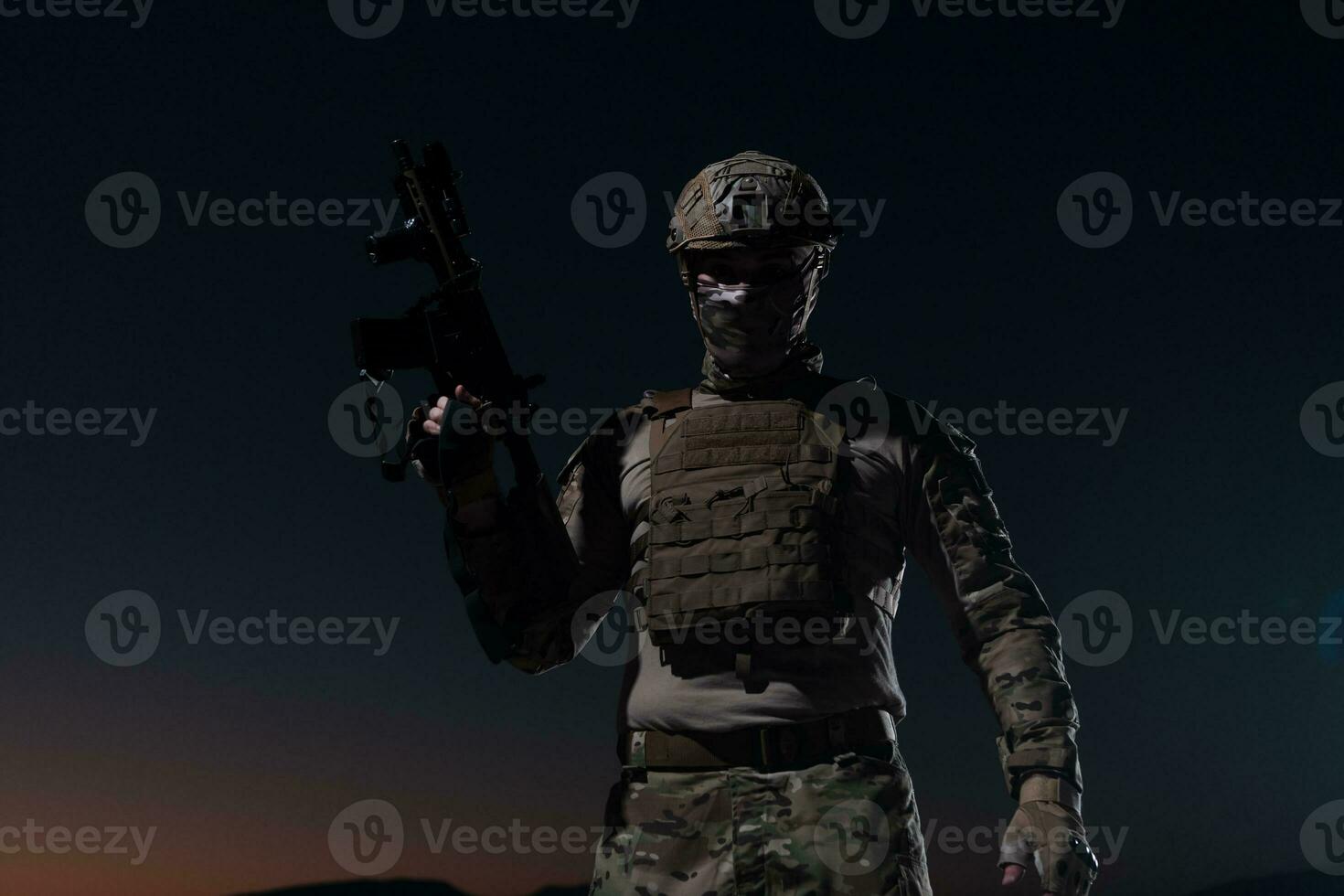 Army soldier in Combat Uniforms with an assault rifle, plate carrier and combat helmet going on a dangerous mission on a rainy night. photo