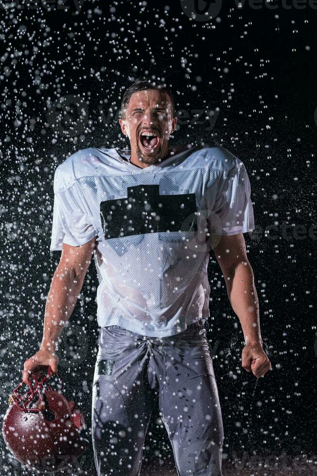 American Football Field Lonely Athlete Warrior Standing on a Field Holds his Helmet and Ready to Play. Player Preparing to Run, Attack and Score Touchdown. Rainy Night with Dramatic Fog, Blue Light photo