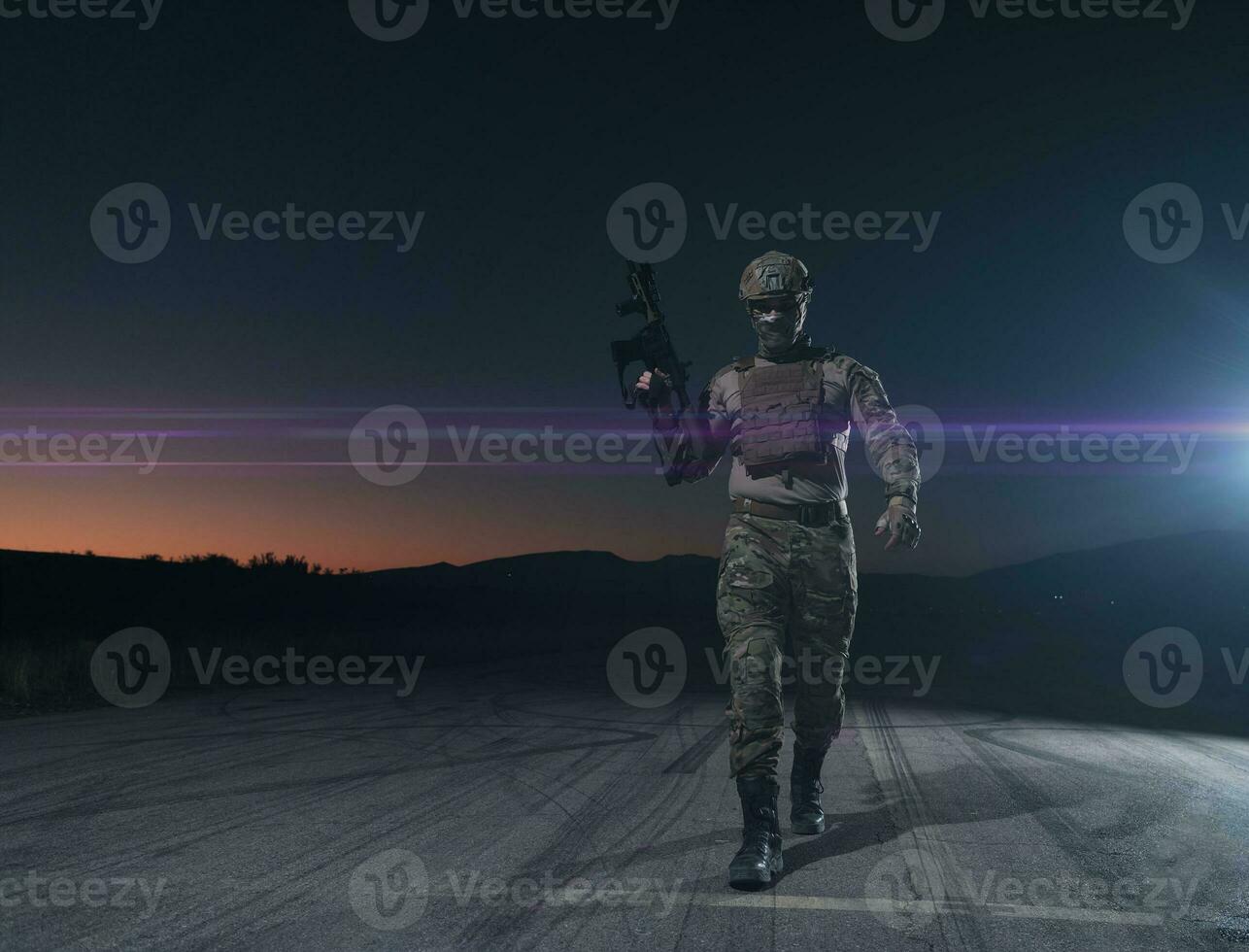 Army soldier in Combat Uniforms with an assault rifle, plate carrier and combat helmet going on a dangerous mission on a rainy night. photo