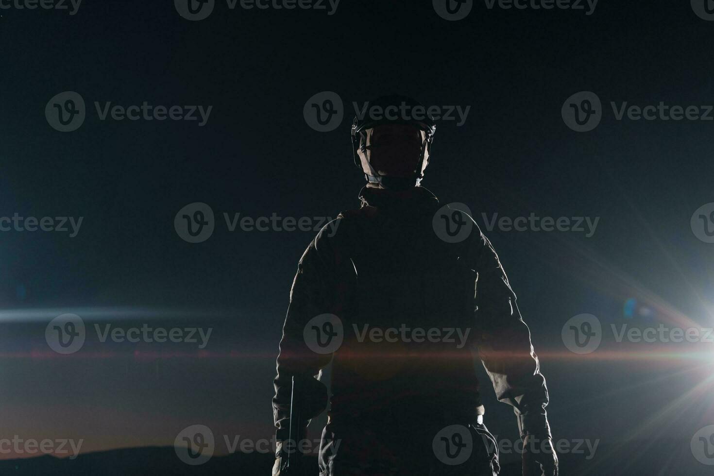 Army soldier in Combat Uniforms with an assault rifle, plate carrier and combat helmet going on a dangerous mission on a rainy night. photo