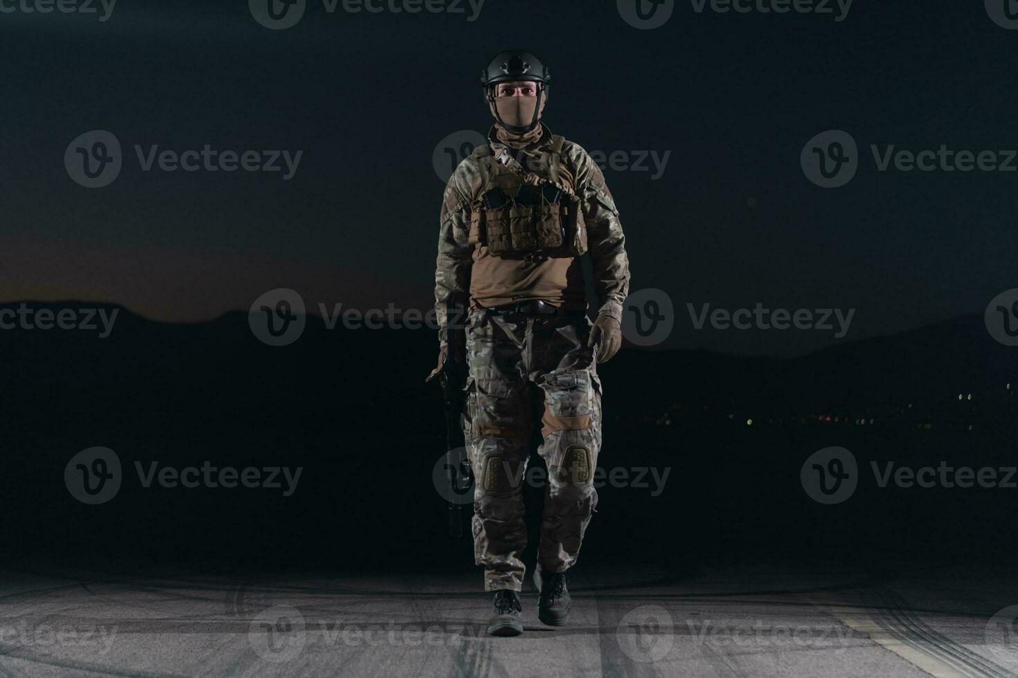 Army soldier in Combat Uniforms with an assault rifle, plate carrier and combat helmet going on a dangerous mission on a rainy night. photo