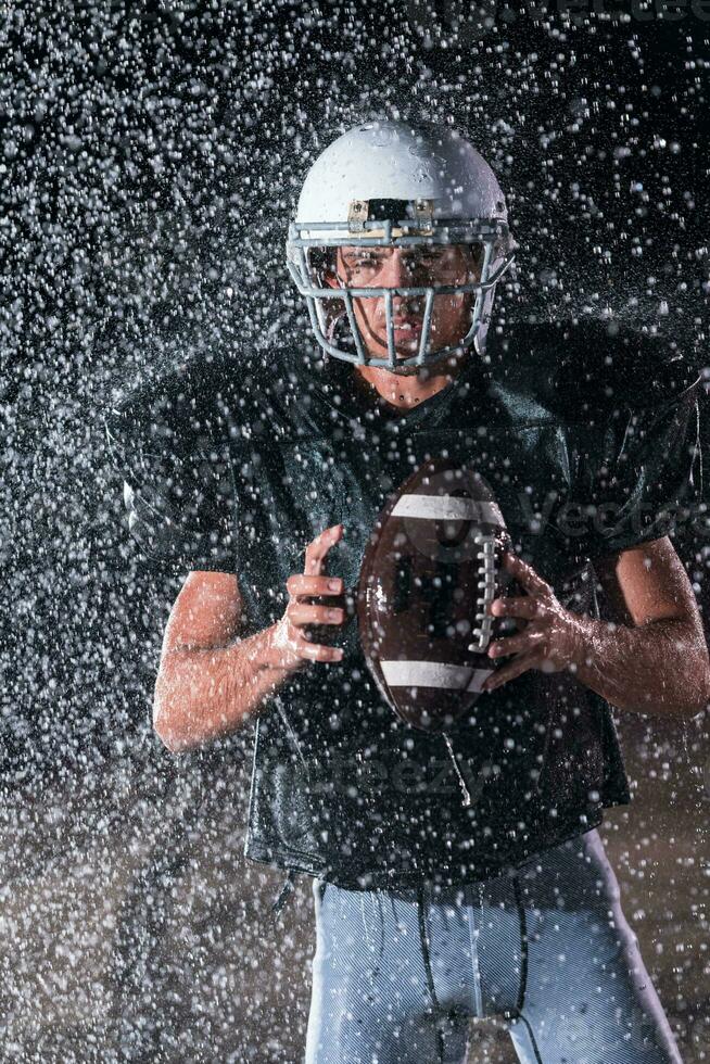 American Football Field Lonely Athlete Warrior Standing on a Field Holds his Helmet and Ready to Play. Player Preparing to Run, Attack and Score Touchdown. Rainy Night with Dramatic Fog, Blue Light photo